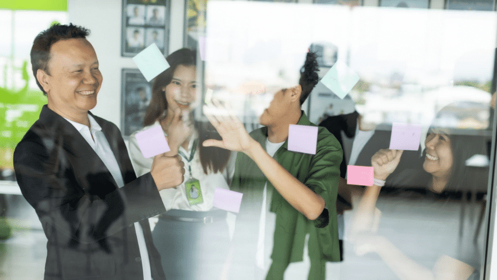 Business team smiling and organizing colorful sticky notes on a glass wall during a creative planning session in the office