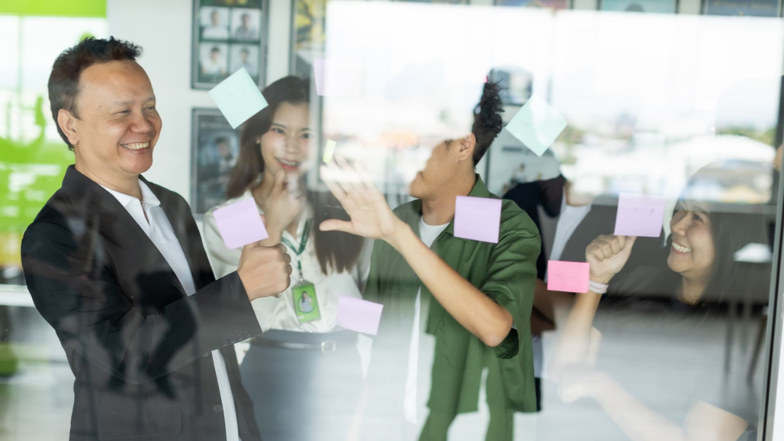 Business team smiling and organizing colorful sticky notes on a glass wall during a creative planning session in the office